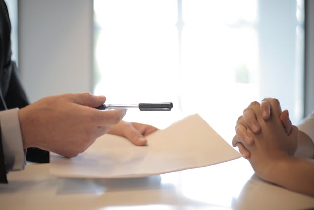 one person holding pen paper other person with their hands crossed